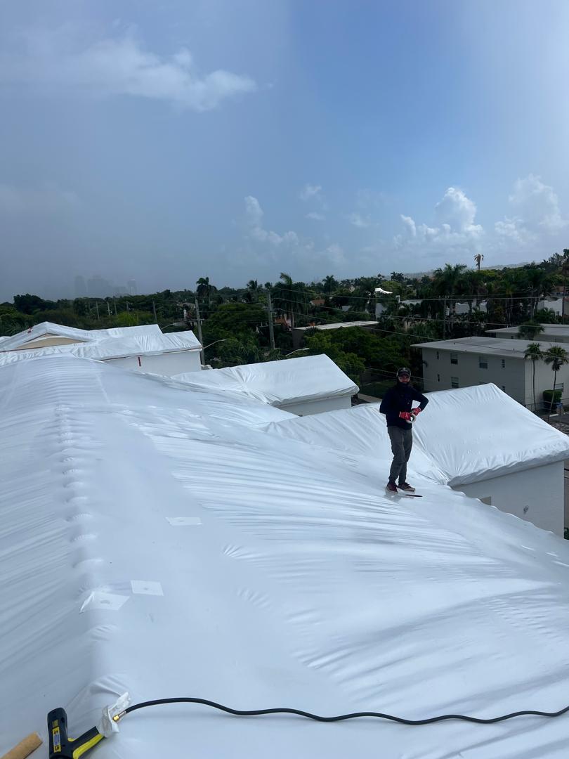 Crew member standing on a freshly covered white roof, city skyline behind